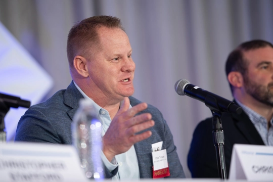 man seated at table speaking into microphone
